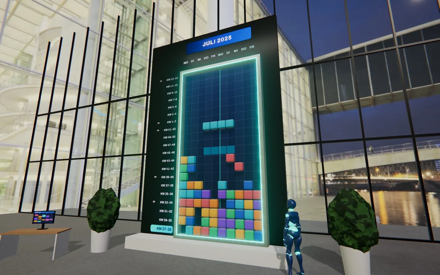 A großer Wandkalender im Büro, auf dem bunte Klebezettl-Stoa zu Reihen gstapelt wern, danebn d'Spielfigur